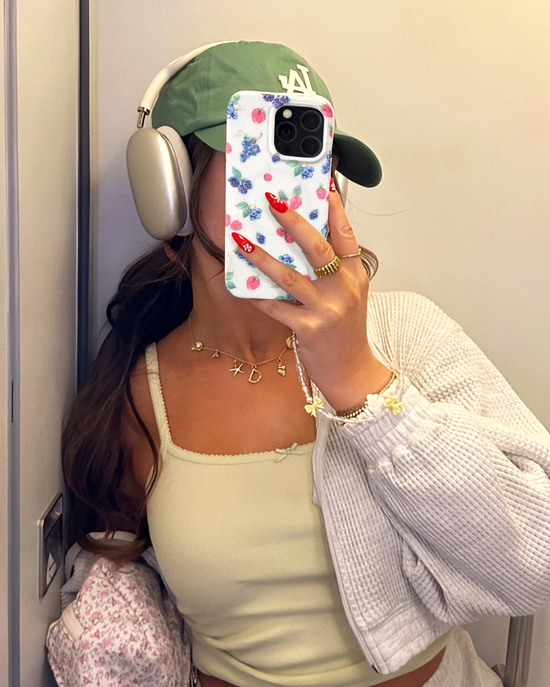 Woman in green cap taking mirror selfie with colorful floral phone case and beaded phone charm