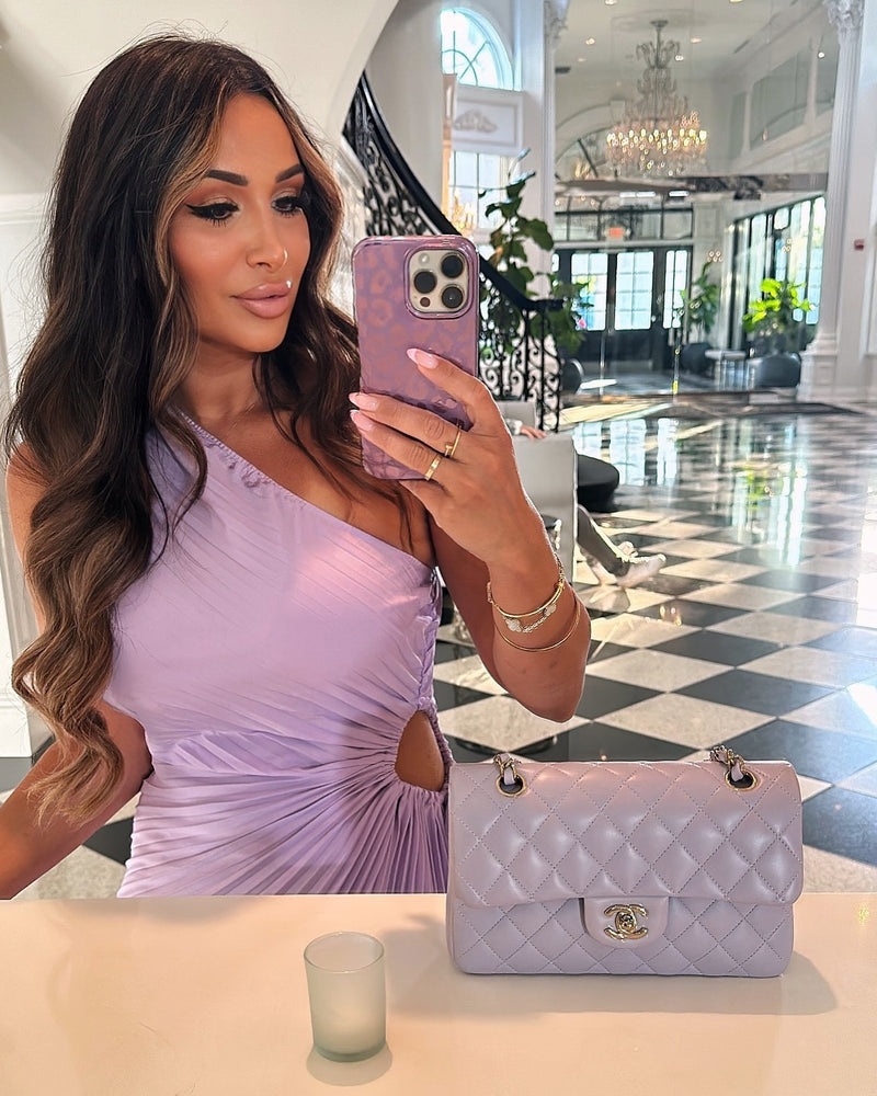 Woman in purple dress taking mirror selfie with quilted phone case in luxury hotel lobby