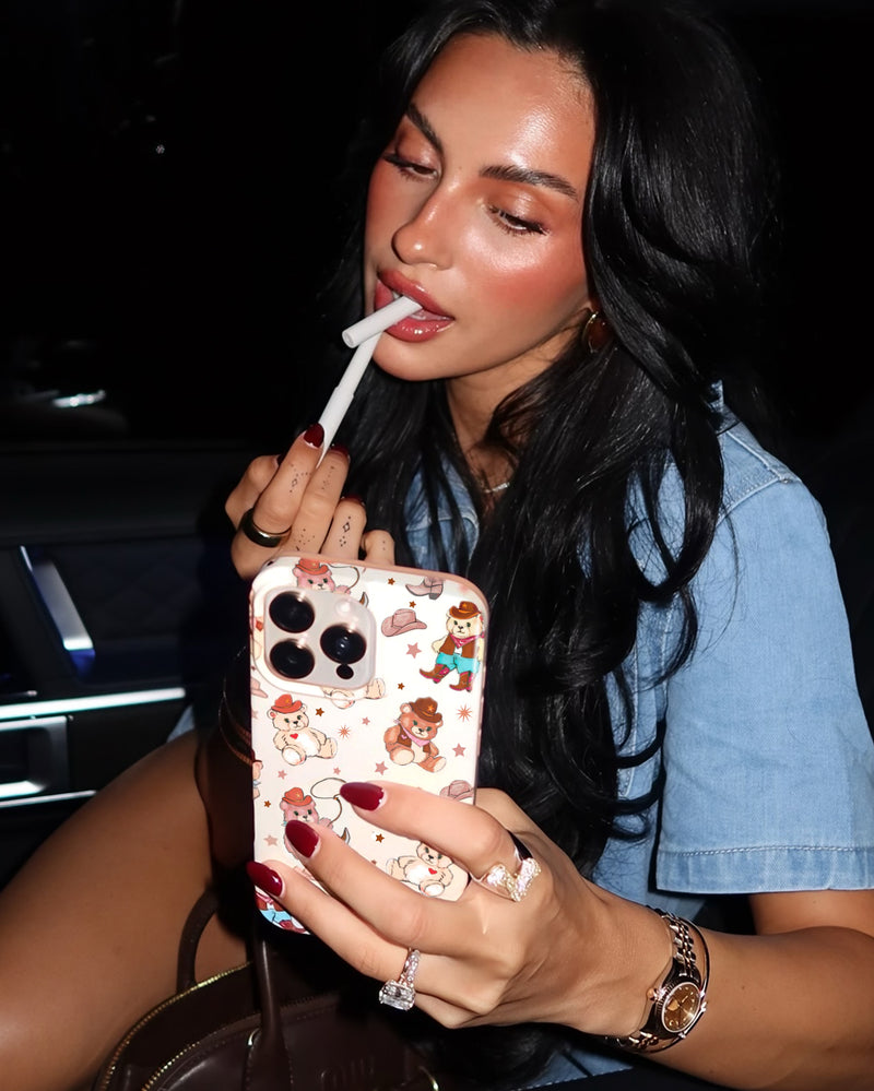 Woman applying lip gloss while holding phone case with bears design